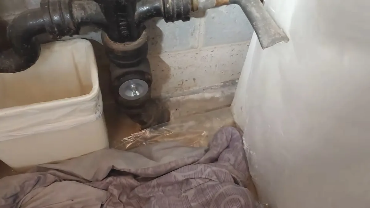 Black cast iron drain and trap rising beside a block wall next to a white tub, with a towel on the floor
