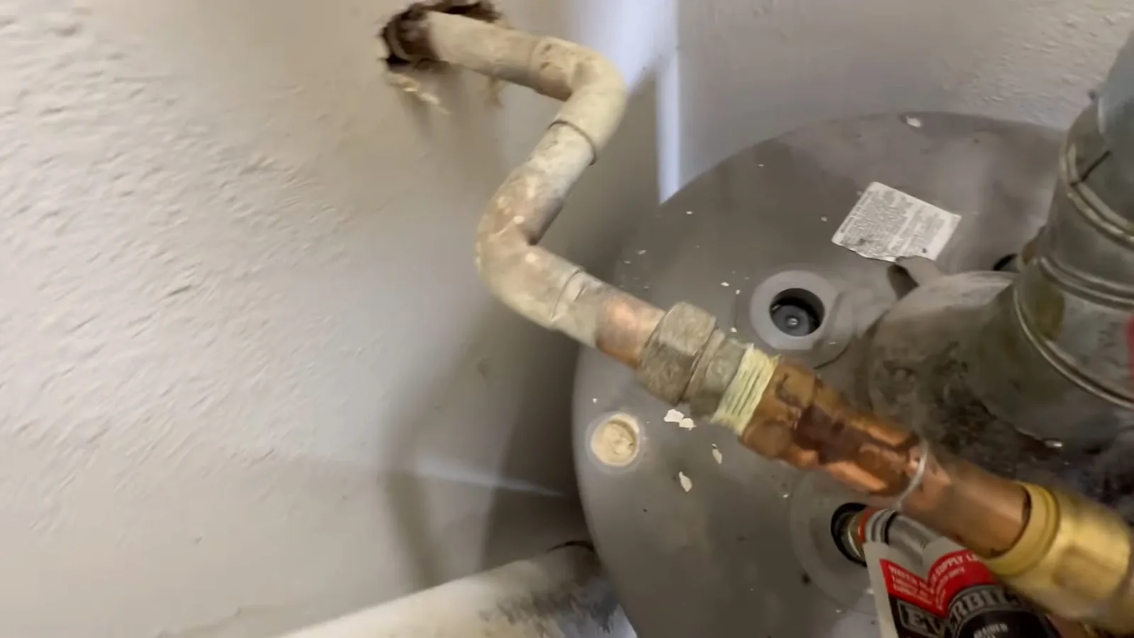 Copper supply pipe and gas fitting meeting the top of a water heater in a corner