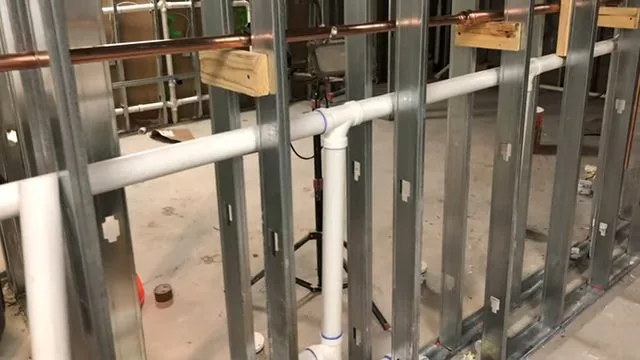 Copper supply lines and white PVC drains running through the openings of a metal stud wall
