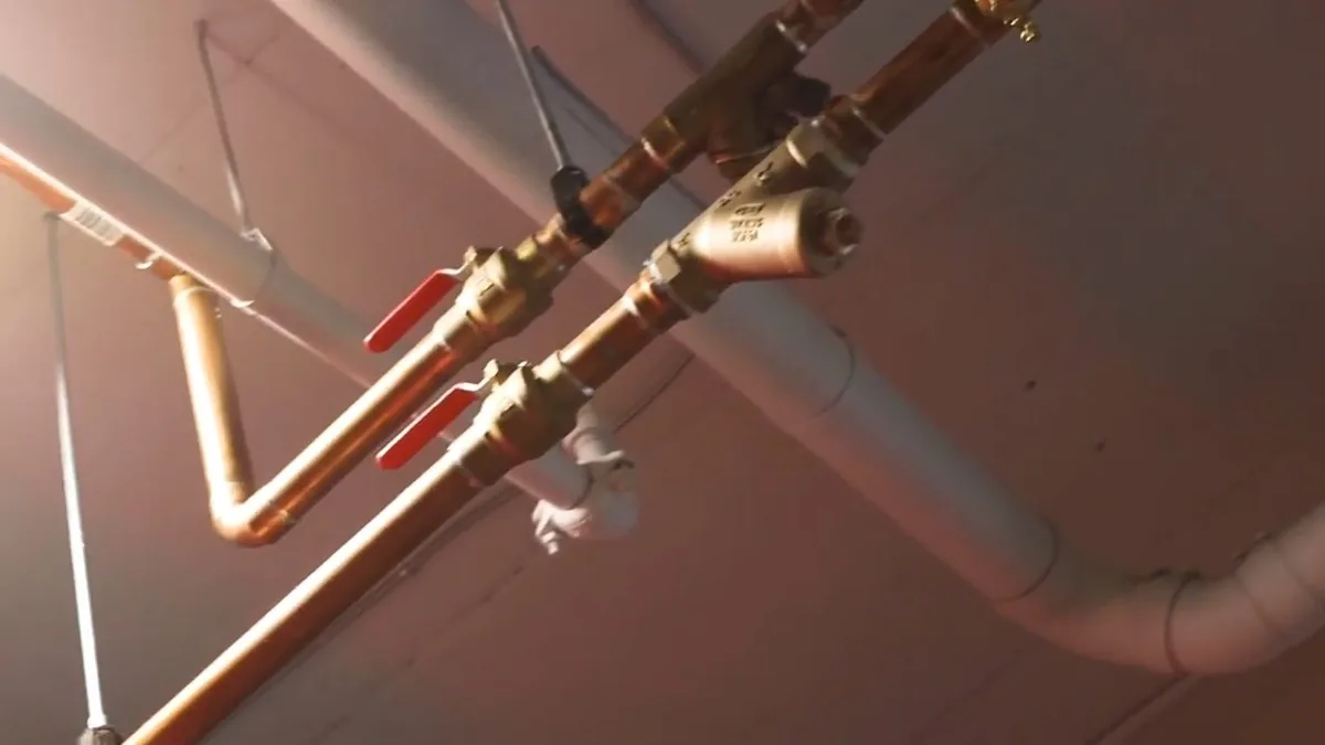 Copper pipes with red-handled ball valves and a strainer running along a ceiling beside a grey pipe