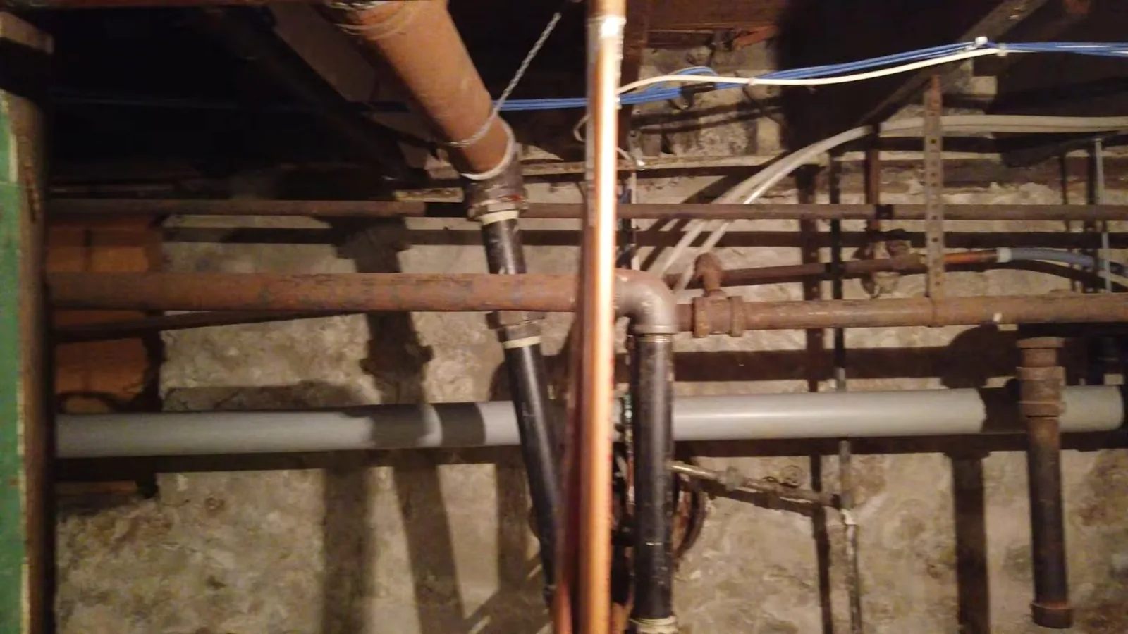 Basement ceiling showing rusted iron, copper and plastic pipes running between joists