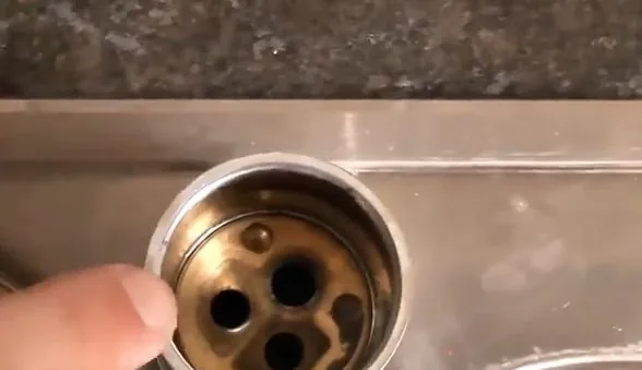 Fingertip beside the brass valve body of a faucet, showing its round water ports
