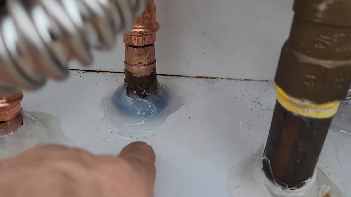 Corrugated flexible connector, copper pipe and a black iron gas pipe with yellow tape rising from a white surface, with a hand beside them
