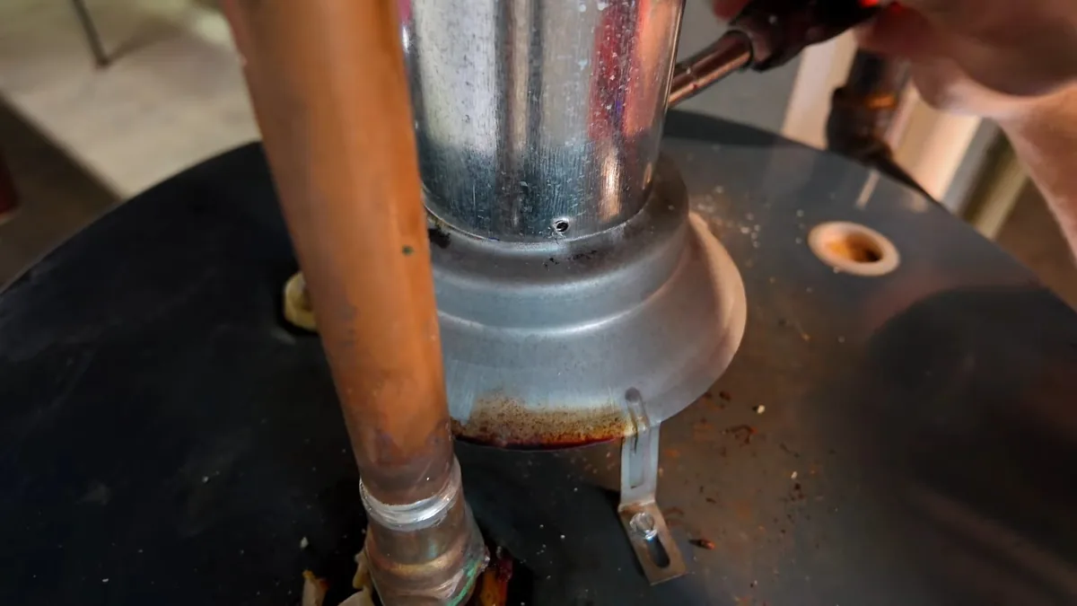 Top of a black water heater with a galvanised flue collar and a copper pipe rising beside it