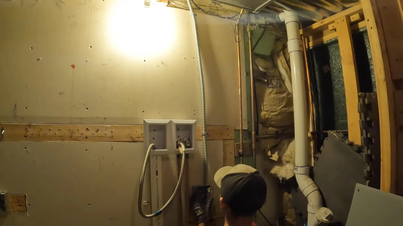 Basement laundry box and white drain pipe in a framed wall, with a person in a cap crouched below