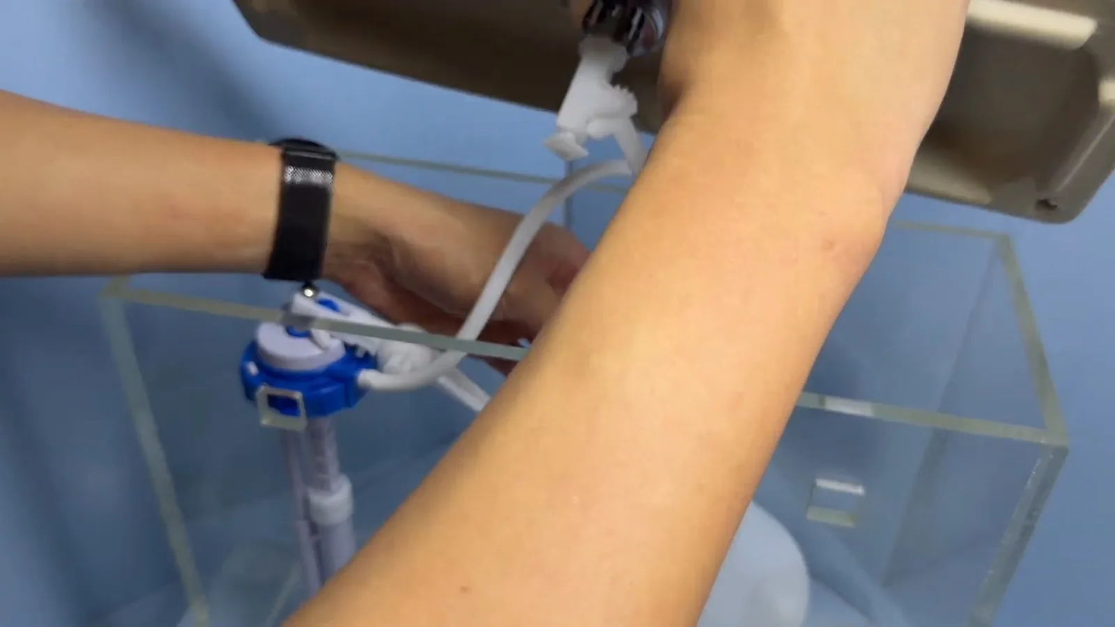 Hands working on the fill valve inside a see-through toilet tank