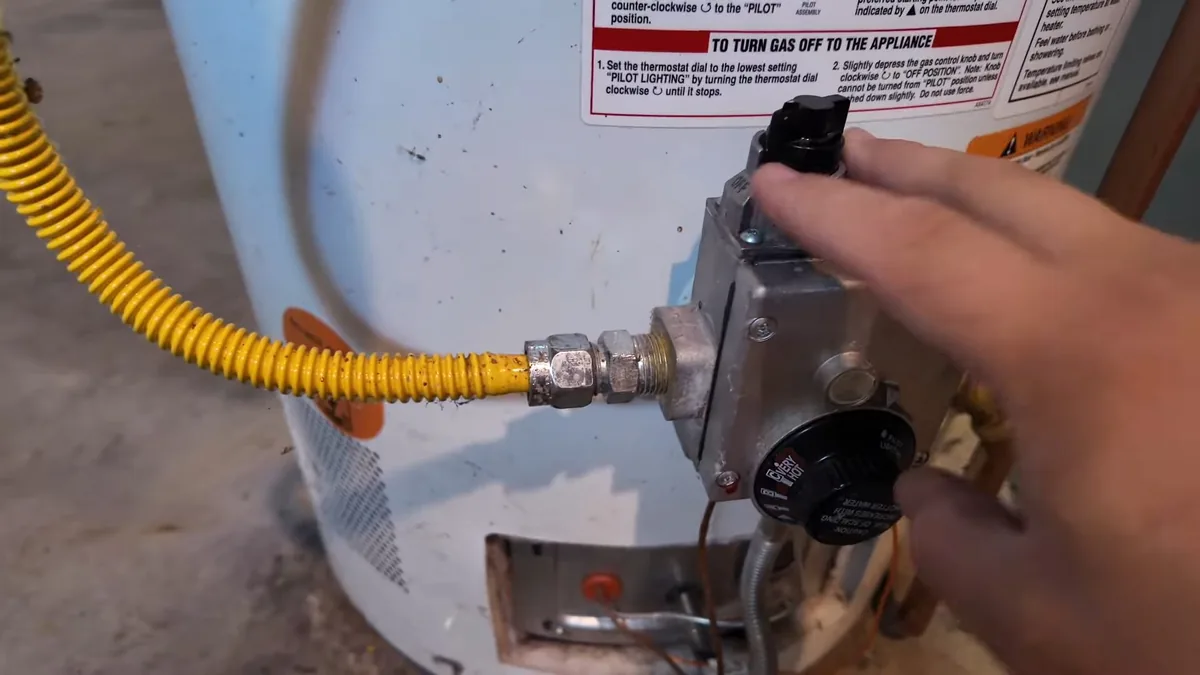 Hand resting on the gas control valve of a water heater, with a yellow flexible gas line attached