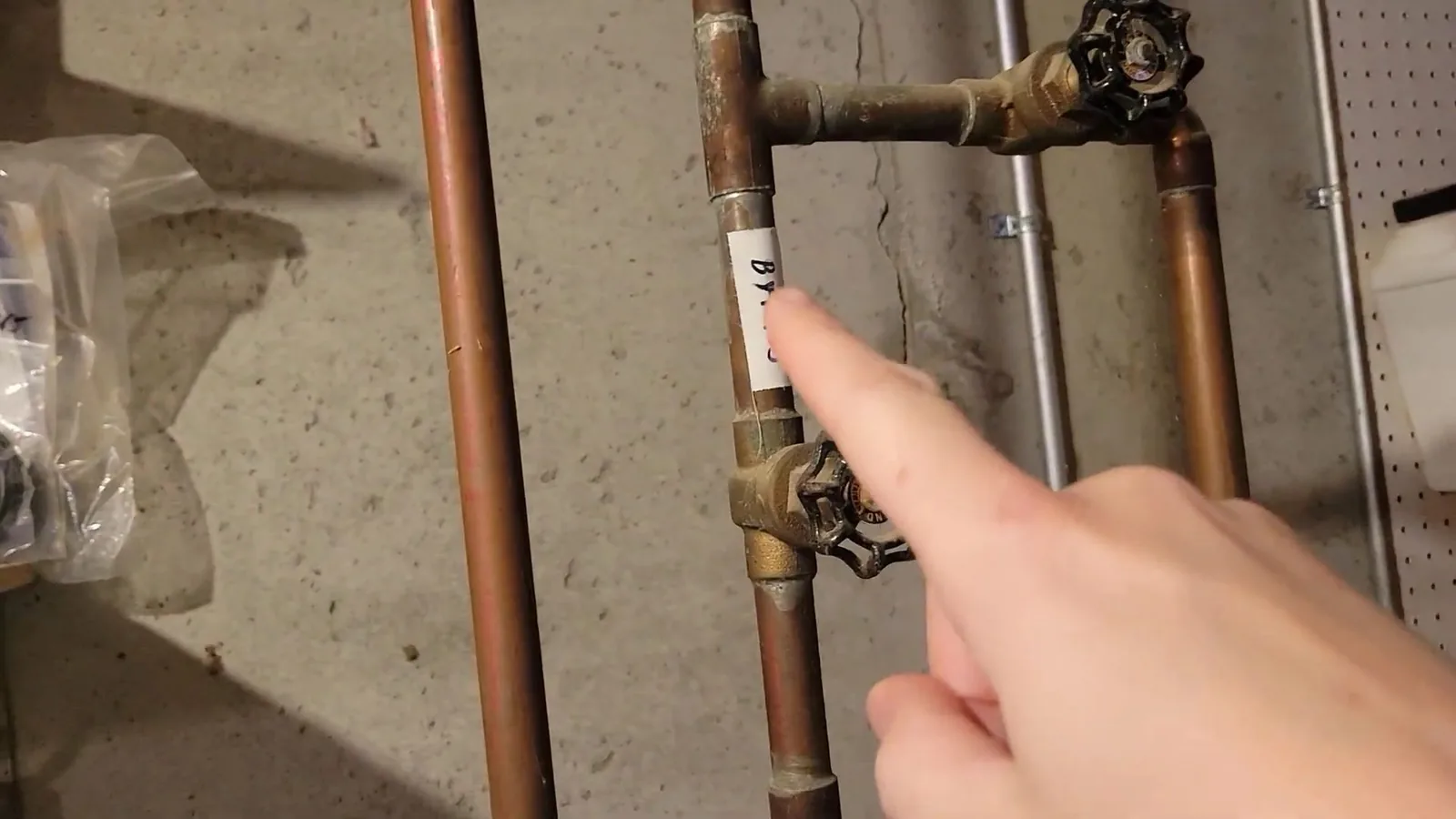 Hand pointing at a gate valve on copper pipes mounted on a basement wall