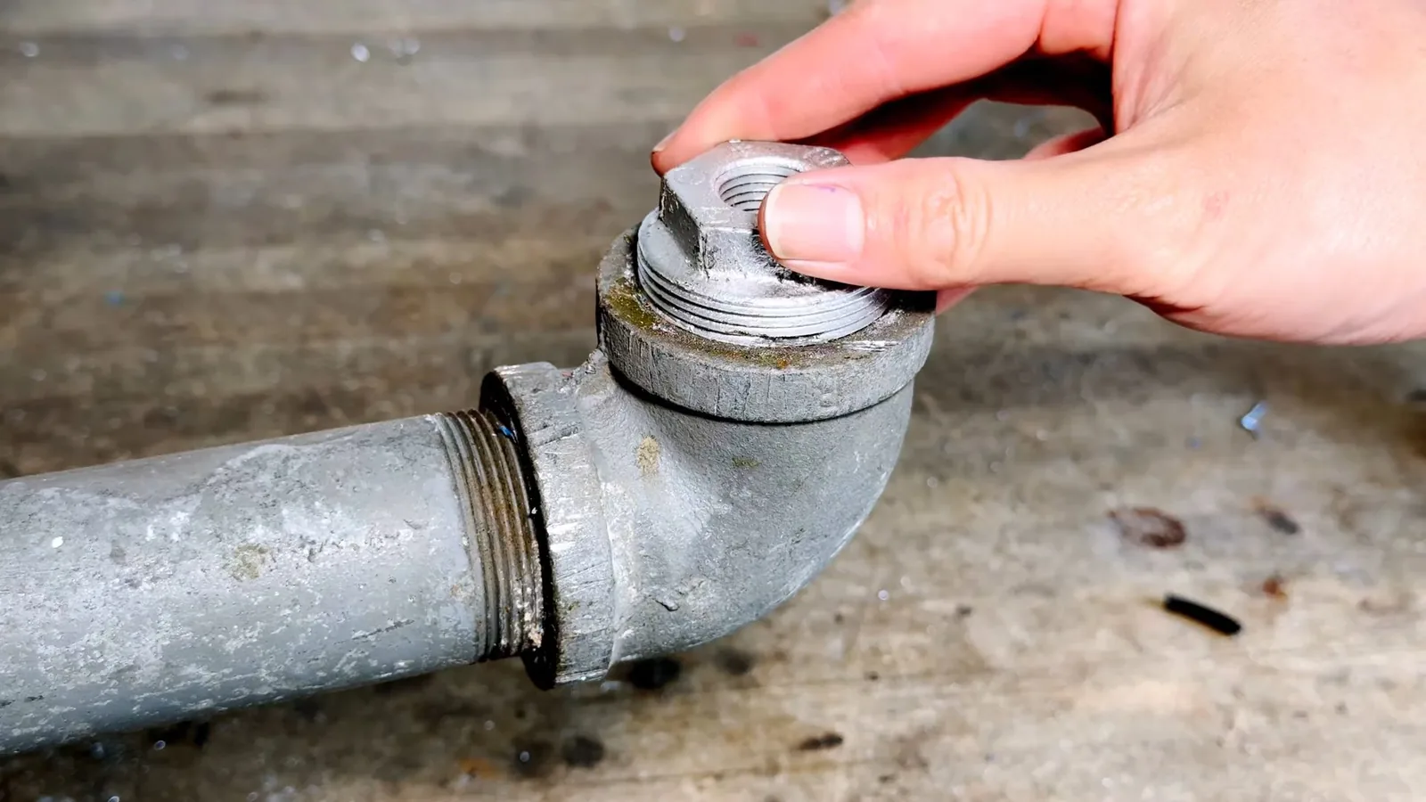Hand turning the cap off a galvanised drain trap sitting on a floor