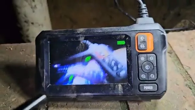 Handheld inspection camera monitor held by a hand, showing the view inside a pipe