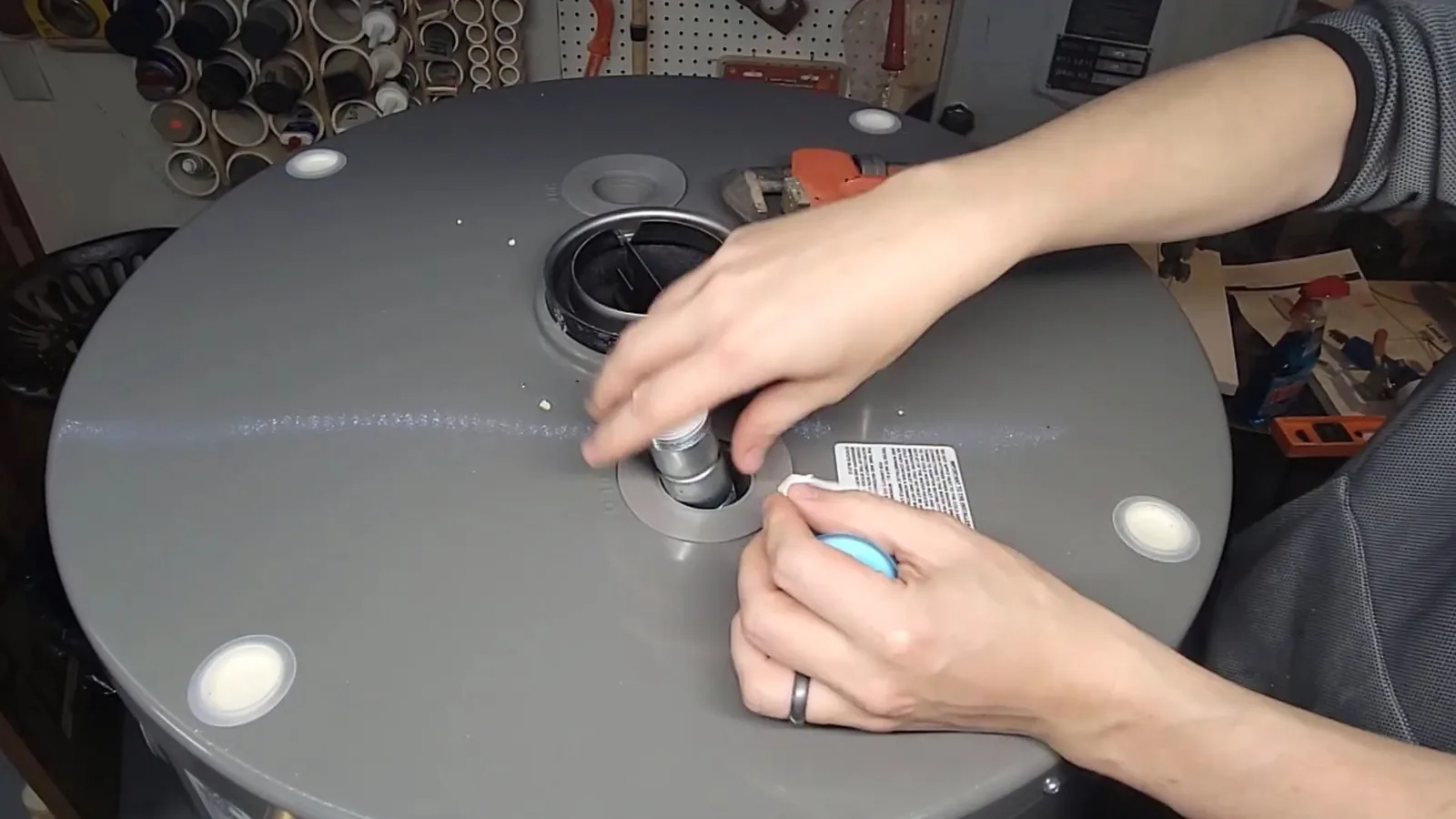 Hands fitting a part into the top of a grey water heater on a workbench