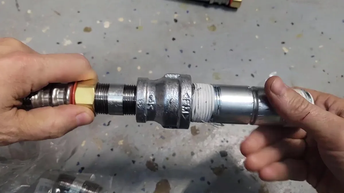 Two hands joining a galvanised threaded fitting to a brass connector on a workshop floor