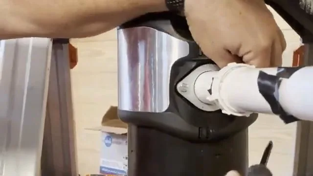 Hands turning the mounting ring of a stainless garbage disposal with a white discharge pipe taped to it