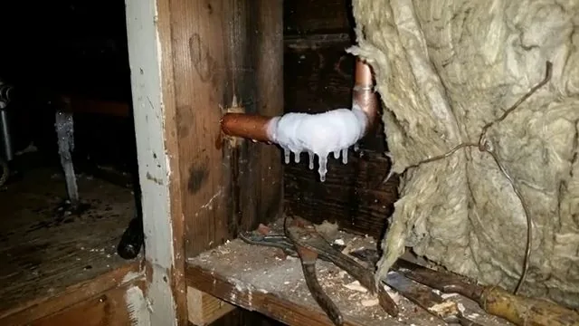 White ice coating a copper elbow inside an insulated wall cavity, with icicles hanging from it