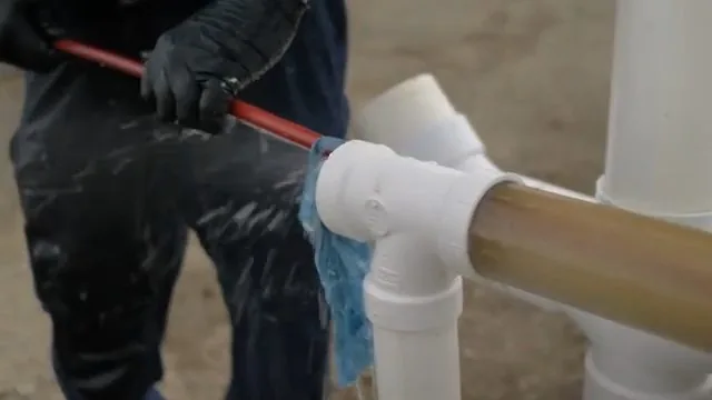 Person in dark clothing feeding a red jetting hose into a white PVC tee, with a blue cloth around the opening and water spraying back