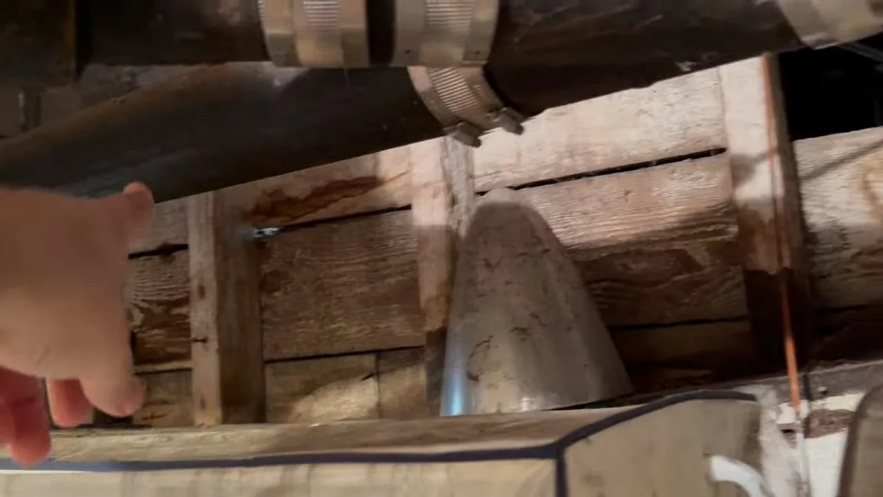 Large old cast iron drain pipe with rubber couplings running under wooden floor boards