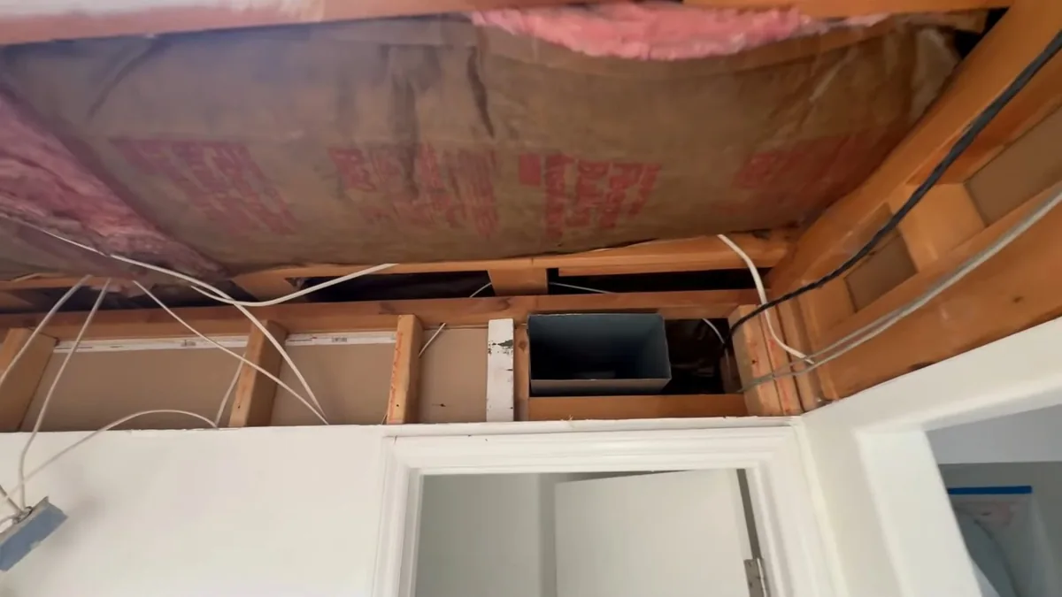 Opened bathroom ceiling above a white doorframe, showing pink insulation, cables and a small duct between joists