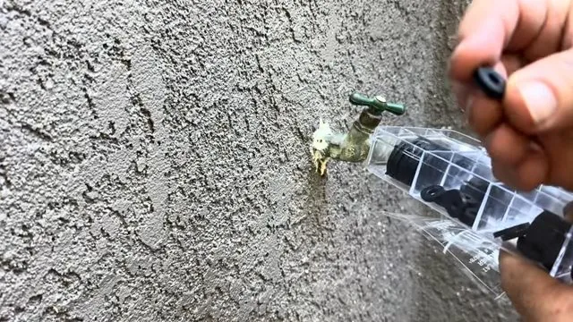 Brass hose bib on a stucco wall with a hand holding a small black washer to it