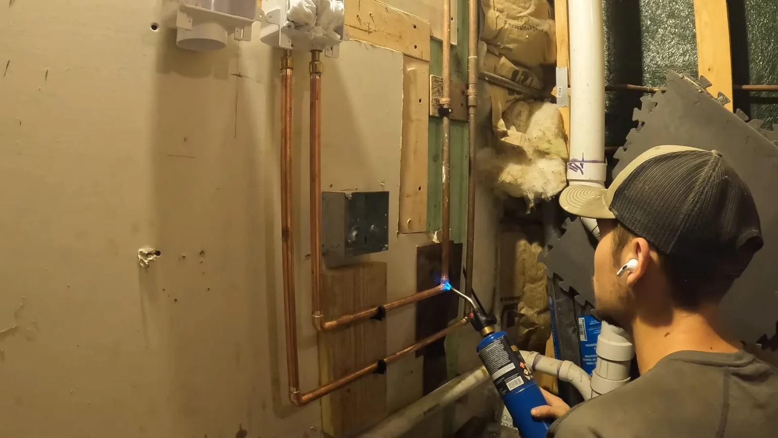 Plumber with a torch working on copper lines in an open utility wall beside a washer box