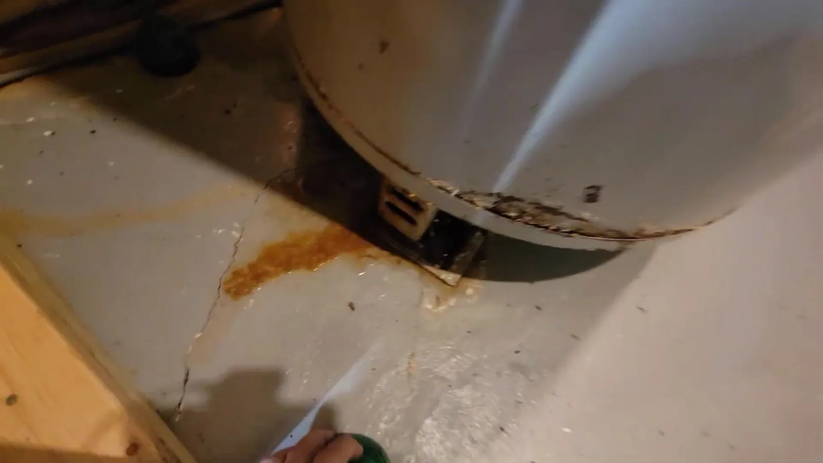 Orange rust stain and damp concrete around the base of a water heater