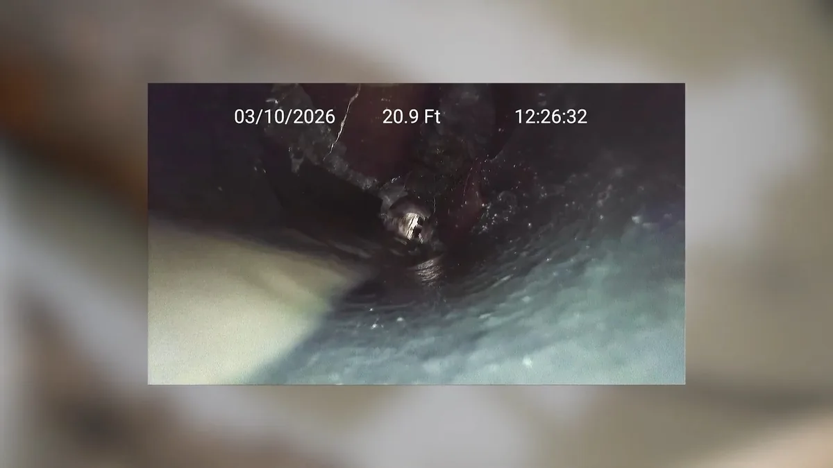 Dark sewer camera view down the inside of a cast iron pipe, with a depth and time readout