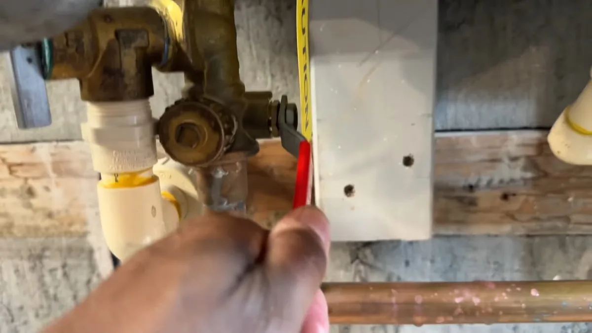 Hand holding a tape measure beside the brass service valve fittings below a tankless heater