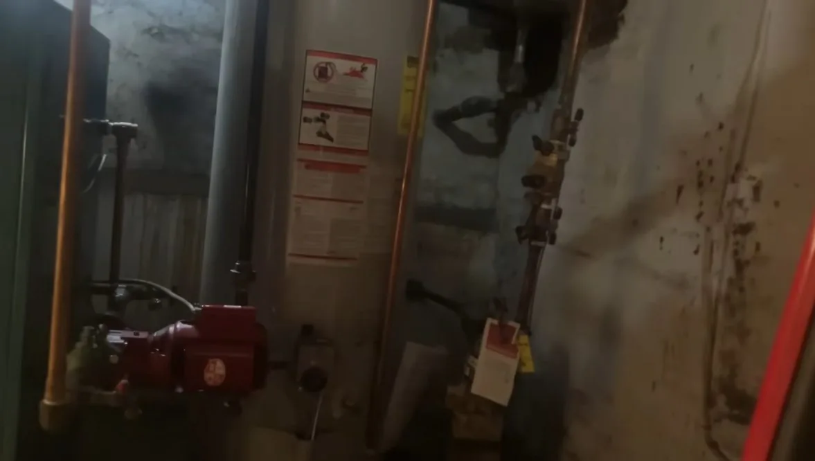 Utility room with copper and iron pipes, a red circulator pump and a warning tag on the wall