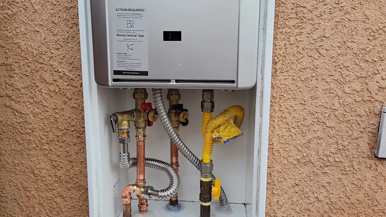Tankless water heater in a recessed wall box on a stucco wall, with copper, gas and flexible lines below