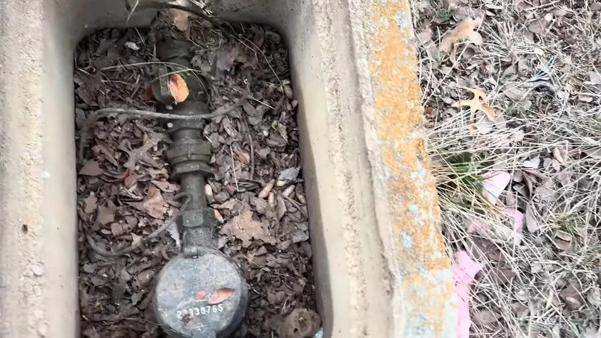 Round water meter and brass valve in a concrete ground box, half covered with dry leaves
