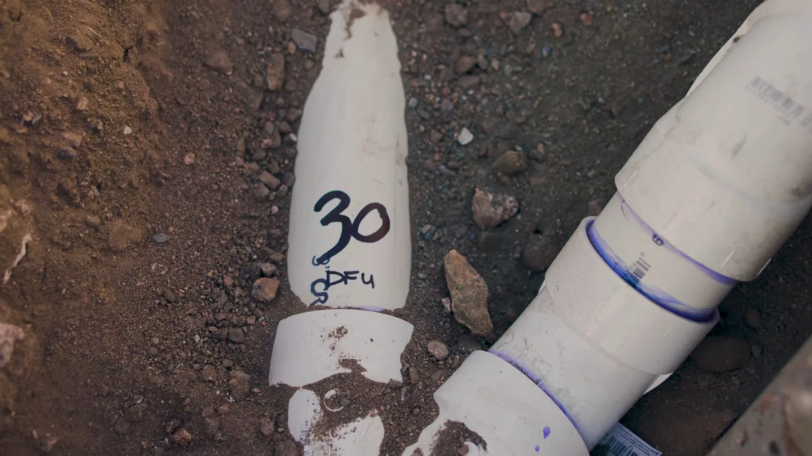 Cut white PVC drain pipes marked with handwritten numbers sitting in open soil