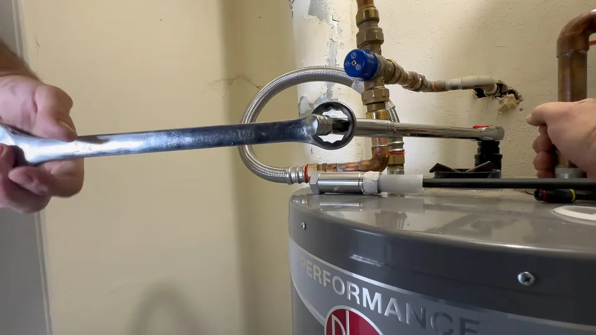 Wrench tightening a flexible supply line on top of a gas water heater, with a blue valve above